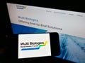Person holding mobile phone with logo of biotechnology company WuXi Biologics (Cayman) Inc. on screen with webpage.