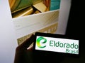 Person holding mobile phone with logo of Brazilian pulp manufacturer Eldorado Brasil Celulose SA on screen with web page.