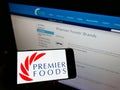 Person holding mobile phone with logo of British food manufacturer Premier Foods plc on screen in front of company website.