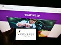 Person holding mobile phone with logo of British foodservice company Compass Group plc on screen in front of webpage.