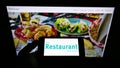 Person holding mobile phone with logo of British gastronomy company The Restaurant Group plc on screen in front of web page.