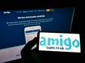 Person holding mobile phone with logo of British loan guarantor Amigo Holdings PLC on screen in front of business web page.