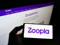 Person holding mobile phone with logo of British real estate platform Zoopla Limited on screen in front of company web page.