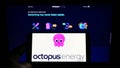 Person holding mobile phone with logo of British renewables company Octopus Energy Group on screen in front of webpage.