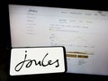 Person holding mobile phone with logo of British retail company Joules Group plc on screen in front of business web page.