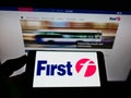 Person holding mobile phone with logo of British transport company FirstGroup plc on screen in front of business web page.