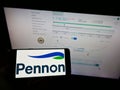 Person holding mobile phone with logo of British water utility company Pennon Group plc on screen in front of web page.