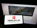 Person holding mobile phone with logo of Canadian company Triple Flag Precious Metals Corp. on screen in front of web page.