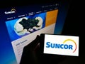 Person holding mobile phone with logo of Canadian oil and gas company Suncor Energy Inc. on screen in front of web page.