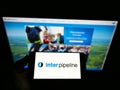 Person holding mobile phone with logo of Canadian oil infrastructure company Inter Pipeline on screen in front of web page.