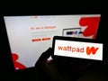 Person holding mobile phone with logo of Canadian self-publishing platform Wattpad on display in front of company web page.