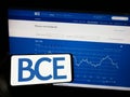 Person holding mobile phone with logo of Canadian telecommunications company BCE Inc. on screen in front of web page.