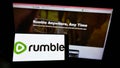 Person holding mobile phone with logo of Canadian video platform company Rumble Inc. on screen in front of web page. Royalty Free Stock Photo