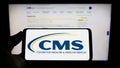 Person holding mobile phone with logo of Centers for Medicare and Medicaid Services (CMS) on screen with web page. Royalty Free Stock Photo