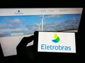 Person holding mobile phone with logo of Centrais ElÃÂ©tricas Brasileiras S.A. (Eletrobras) on screen with web page. Royalty Free Stock Photo