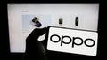 Person holding mobile phone with logo of Chinese consumer electronics company OPPO on screen in front of business webpage.