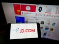 Person holding mobile phone with logo of Chinese e-commerce company JD.com Inc. on screen in front of online shop.