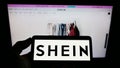 Person holding mobile phone with logo of Chinese e-commerce company Shein on screen in front of business web page. Royalty Free Stock Photo