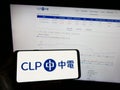 Person holding mobile phone with logo of Chinese energy company CLP Group on screen in front of business web page.