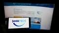 Person holding mobile phone with logo of Chinese submarine network company HMN Tech on screen in front of business web page.
