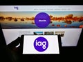 Person holding mobile phone with logo of company Insurance Australia Group Limited (IAG) on screen in front of webpage.