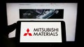 Person holding mobile phone with logo of company Mitsubishi Materials Corporation (MMC) on screen in front of web page. Royalty Free Stock Photo