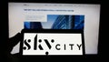 Person holding mobile phone with logo of company SkyCity Entertainment Group Limited on screen in front of web page.