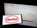 Person holding mobile phone with logo of consumer goods company Henkel AG Co. KGaA on screen in front of business web page. Royalty Free Stock Photo