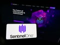 Person holding mobile phone with logo of cybersecurity firm Sentinel Labs Inc. (SentinelOne) on screen with web page.