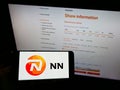 Person holding mobile phone with logo of Dutch insurance company NN Group N.V. on screen in front of business web page.