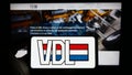 Person holding mobile phone with logo of Dutch manufacturing company VDL Groep BV on screen in front of business web page.
