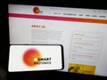 Person holding mobile phone with logo of Dutch semiconductor company SMART Photonics BV on screen in front of web page.