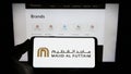 Person holding mobile phone with logo of Emirati company Majid Al Futtaim Group on screen in front of business web page.