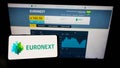 Person holding mobile phone with logo of financial services company Euronext N.V. on screen in front of business web page.