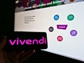 Person holding mobile phone with logo of Franch media conglomerate Vivendi SA on screen in front of website.