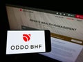 Person holding mobile phone with logo of Franco-German financial company Oddo BHF AG on screen in front of business website.