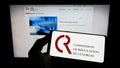 Person holding mobile phone with logo of French Commission de Regulation de l\'Energie (CRE) on screen.