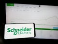 Person holding mobile phone with logo of French company Schneider Electric SE on screen in front of business web page. Royalty Free Stock Photo