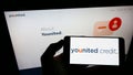 Person holding mobile phone with logo of French financial platform company Younited Credit on screen in front of web page.