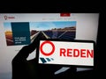 Person holding mobile phone with logo of French photovoltaic company Reden Solar S.A.S. on screen in front of web page.