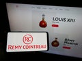 Person holding mobile phone with logo of French spirits company RÃÂ©my Cointreau S.A. on screen in front of business web page. Royalty Free Stock Photo