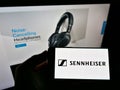 Person holding mobile phone with logo of German audio company Sennheiser electronic on screen in front of business website.