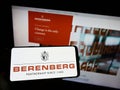 Person holding mobile phone with logo of German bank Joh. Berenberg, Gossler Co. KG on screen in front of web page. Royalty Free Stock Photo