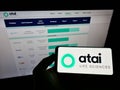 Person holding mobile phone with logo of German biotech company ATAI Life Sciences AG on screen in front of business webpage.