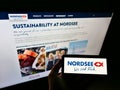Person holding mobile phone with logo of German fast-food restaurant chain Nordsee GmbH on display in front of web page.