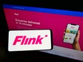 Person holding mobile phone with logo of German grocery delivery company Flink SE on screen in front of business web page.