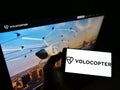 Person holding mobile phone with logo of German helicopter manufacturer Volocopter GmbH on screen in front of web page.