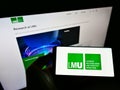 Person holding mobile phone with logo of German Ludwig Maximilian University of Munich on screen in front of website.