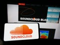 Person holding mobile phone with logo of German music sharing company SoundCloud on screen in front of business web page.