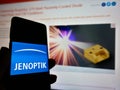 Person holding mobile phone with logo of German photonics company Jenoptik AG on display in front of web page.